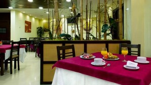 Un espace repas avec des tables préparées pour le petit-déjeuner, proposant une variété de plats et de boissons.