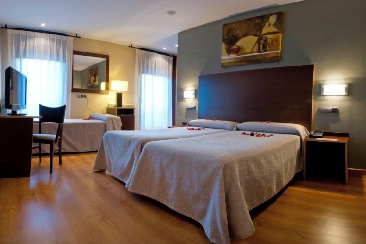 A hotel room with two beds, a desk, a chair, and a painting on the wall.