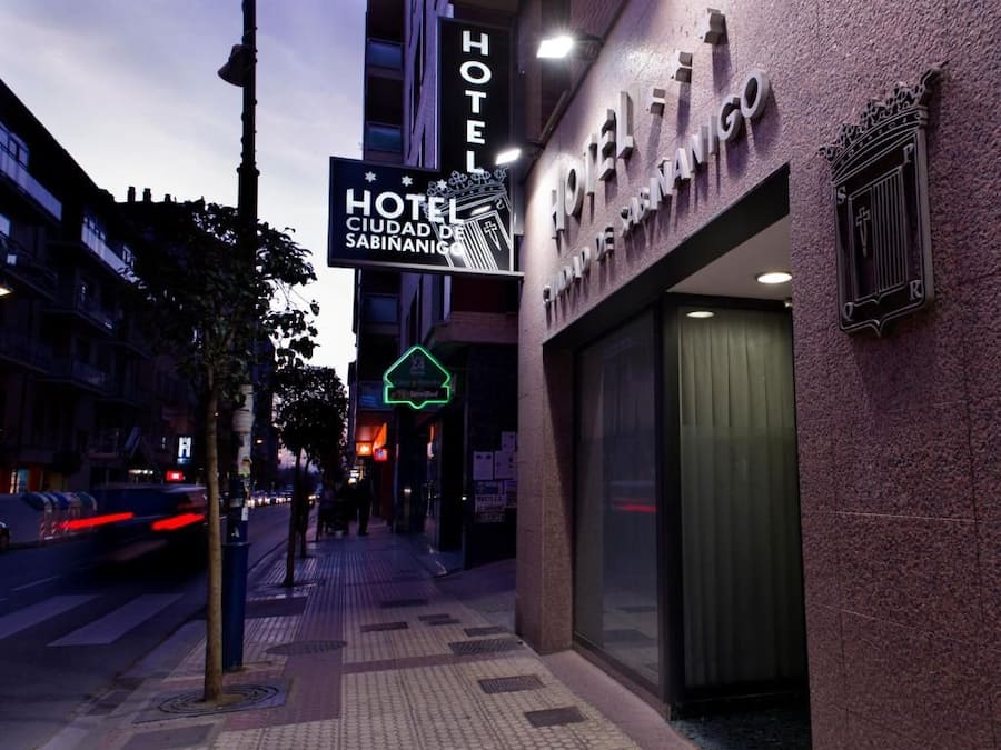 Entrada de un hotel con un cartel que indica 'HOTEL CIUDAD DE SABINANICO' y un letrero de neón que dice 'HOTEL DE SAN MIGUEL'.