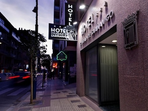Een hotel ingang met een bord waarop 'HOTEL CIUDAD DE SABINANICO' staat en een neonreclame voor 'HOTEL DE SAN MIGUEL'.