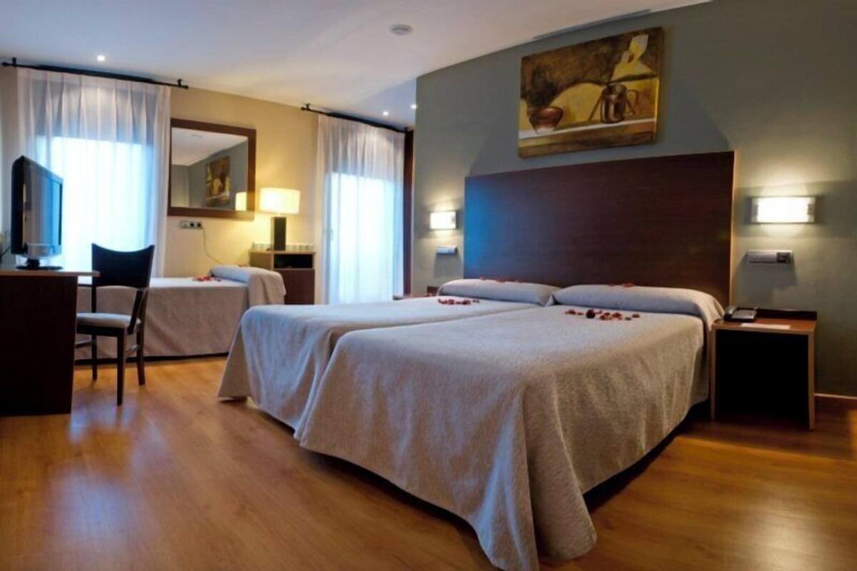Une chambre d’hôtel avec deux lits, un bureau, une chaise et un tableau au mur.