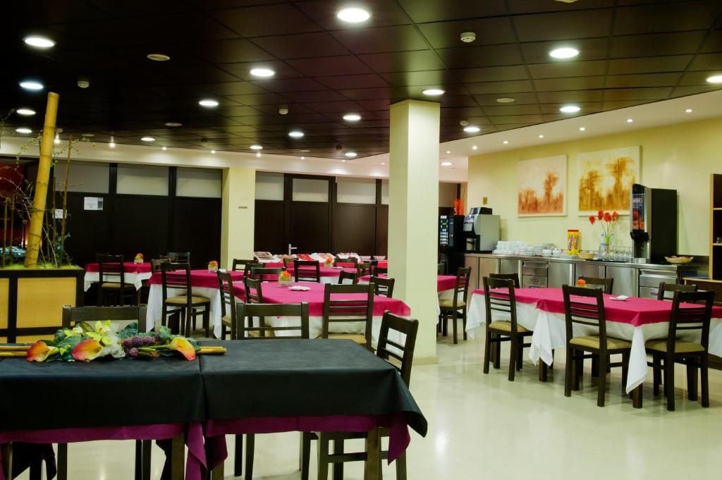 Un espace repas avec des tables disposées pour accueillir plusieurs personnes, un coin cuisine équipé d’appareils électroménagers et des œuvres d’art accrochées aux murs.