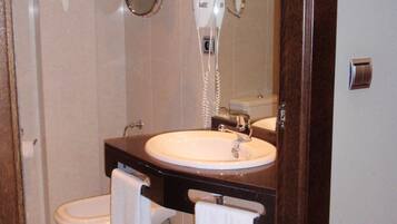 Un baño con lavamanos blanco, inodoro, secador de pelo y espejo.