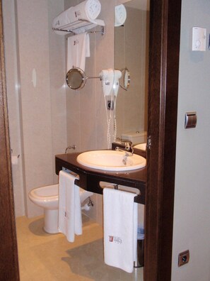 Une salle de bain avec un lavabo blanc, des toilettes, un sèche-cheveux et un miroir.