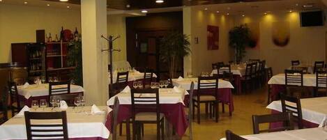 A restaurant with multiple tables and chairs, each set with a white tablecloth and wine glasses.