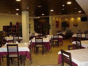 A restaurant with multiple tables and chairs, each covered with a white tablecloth and a red table runner. - Snö Ciudad de Sabiñanigo (Sabinanigo)