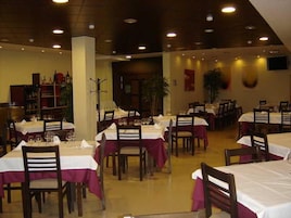 Un restaurante con varias mesas y sillas, cada conjunto con mantel blanco y copas de vino.
