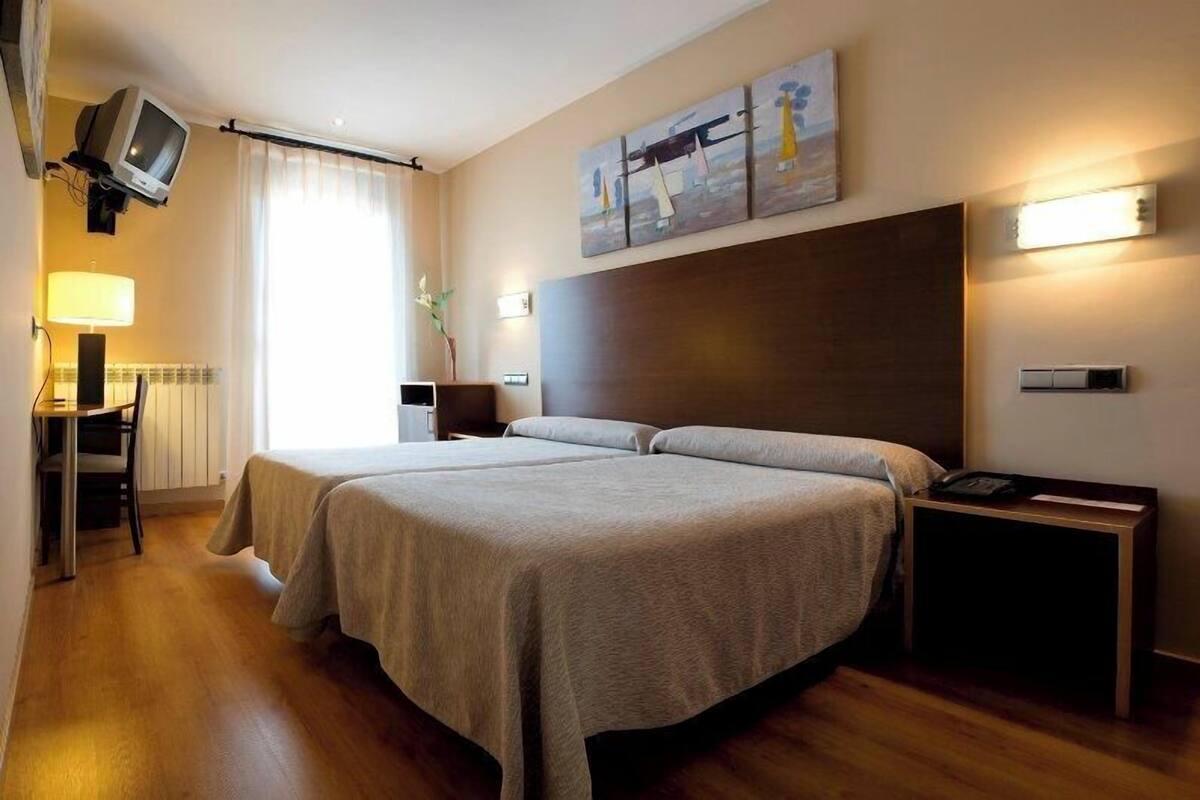 Une chambre d’hôtel avec deux lits, un bureau avec une lampe, une télévision et des œuvres d’art accrochées au mur.