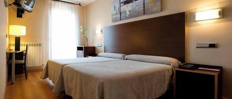 A hotel room with two beds, a desk with a lamp, a television, and artwork on the wall.
