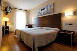 Une chambre d’hôtel avec deux lits, un bureau avec une lampe, une télévision et des œuvres d’art accrochées au mur.