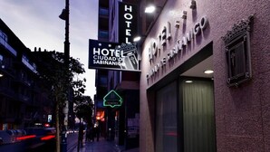 L’entrée d’un hôtel, avec une enseigne indiquant « HÔTEL CIUDAD DE SABINANICO » et un panneau lumineux signalant la présence d’un bar à proximité.