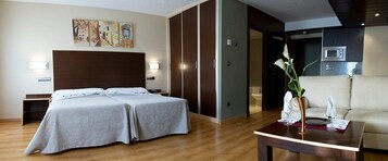 Habitación de hotel con cama doble, sofá, mesa de comedor y zona de cocina.