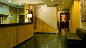 Un espace d’accueil d’hôtel comprenant un comptoir en bois, un bureau de réception, une horloge murale et un panneau indiquant l’emplacement d’un restaurant.