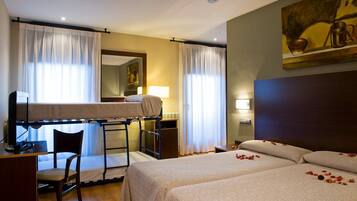 Une chambre d’hôtel avec des lits superposés, un bureau, une chaise et un lit parsemé de pétales de rose.