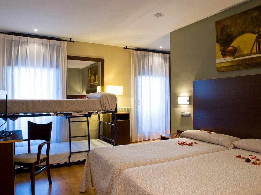 A hotel room with bunk beds, a desk, a chair, and a bed with rose petals.