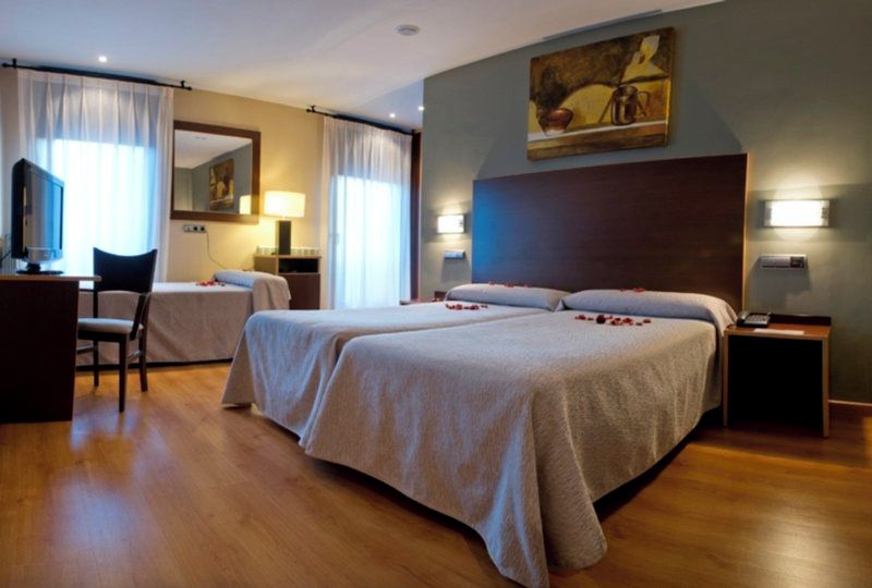 A hotel room with two beds, a desk, a chair, and a painting on the wall.