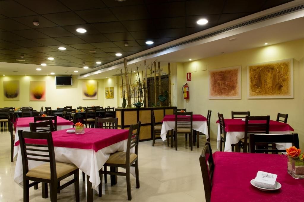 Un área de comedor con mesas dispuestas para el servicio, sillas y una barra con extintor.