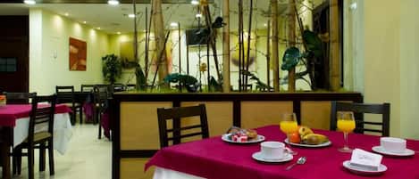 Un comedor con mesas dispuestas para el desayuno, con una variedad de platos y bebidas.