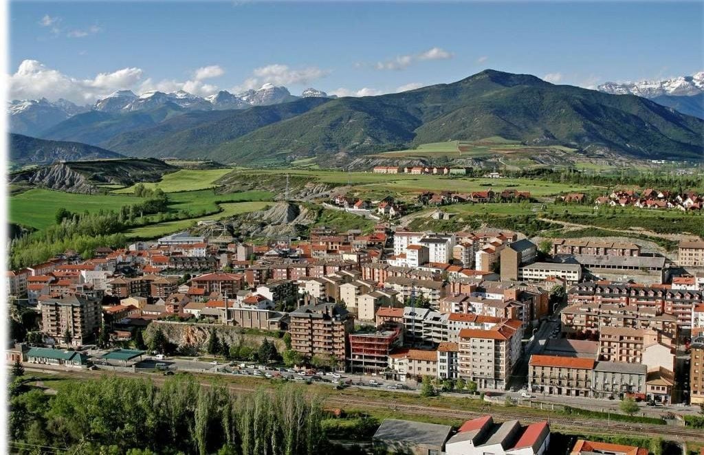 A town with a mix of residential and commercial buildings, surrounded by mountains.