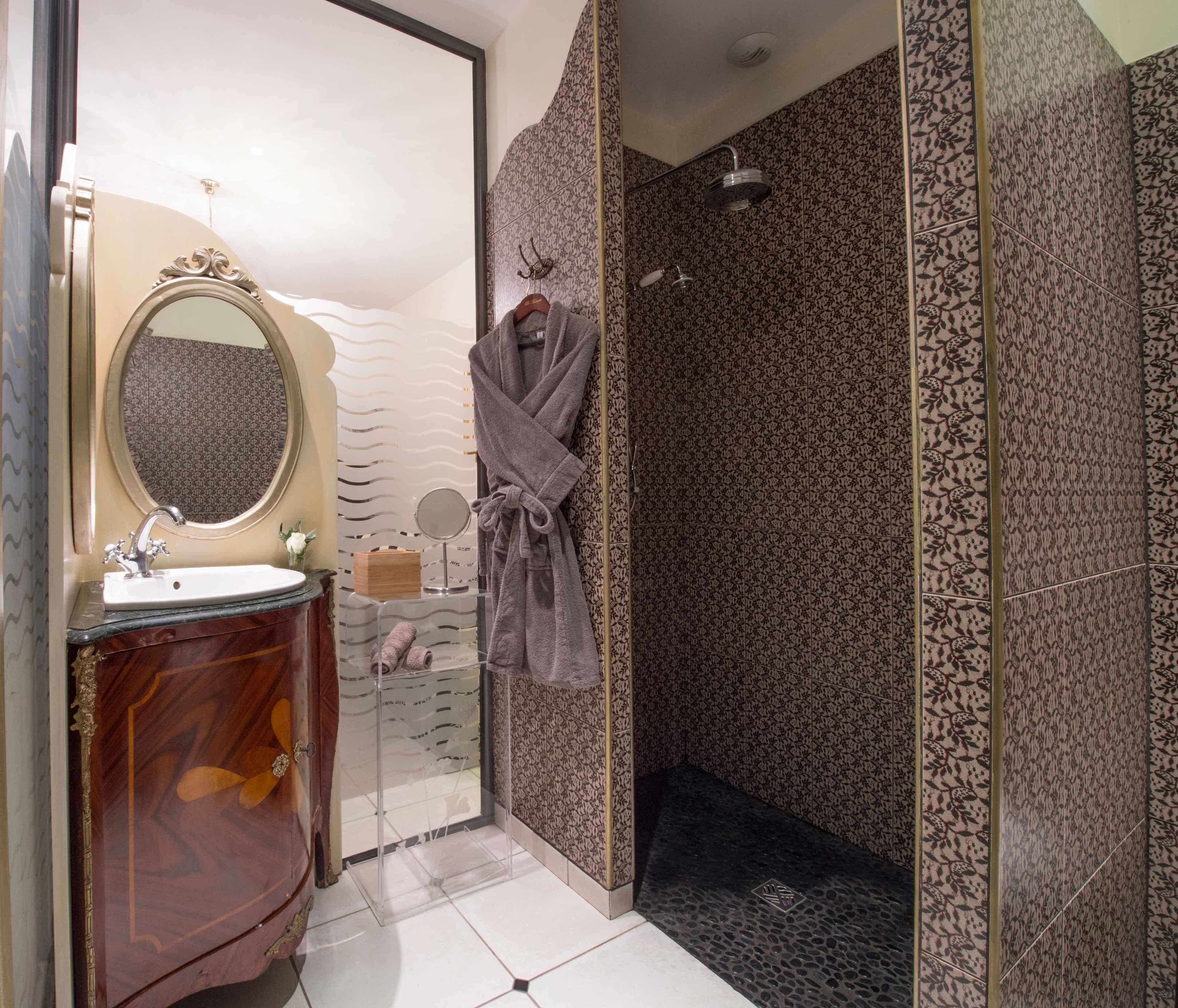 A bathroom with a vanity, a mirror, a robe, a shower, and patterned tiles.