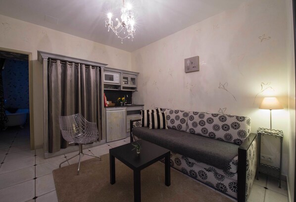 A living room with a sofa, a coffee table, a chair, a chandelier, and a kitchen area with cabinets and a sink.