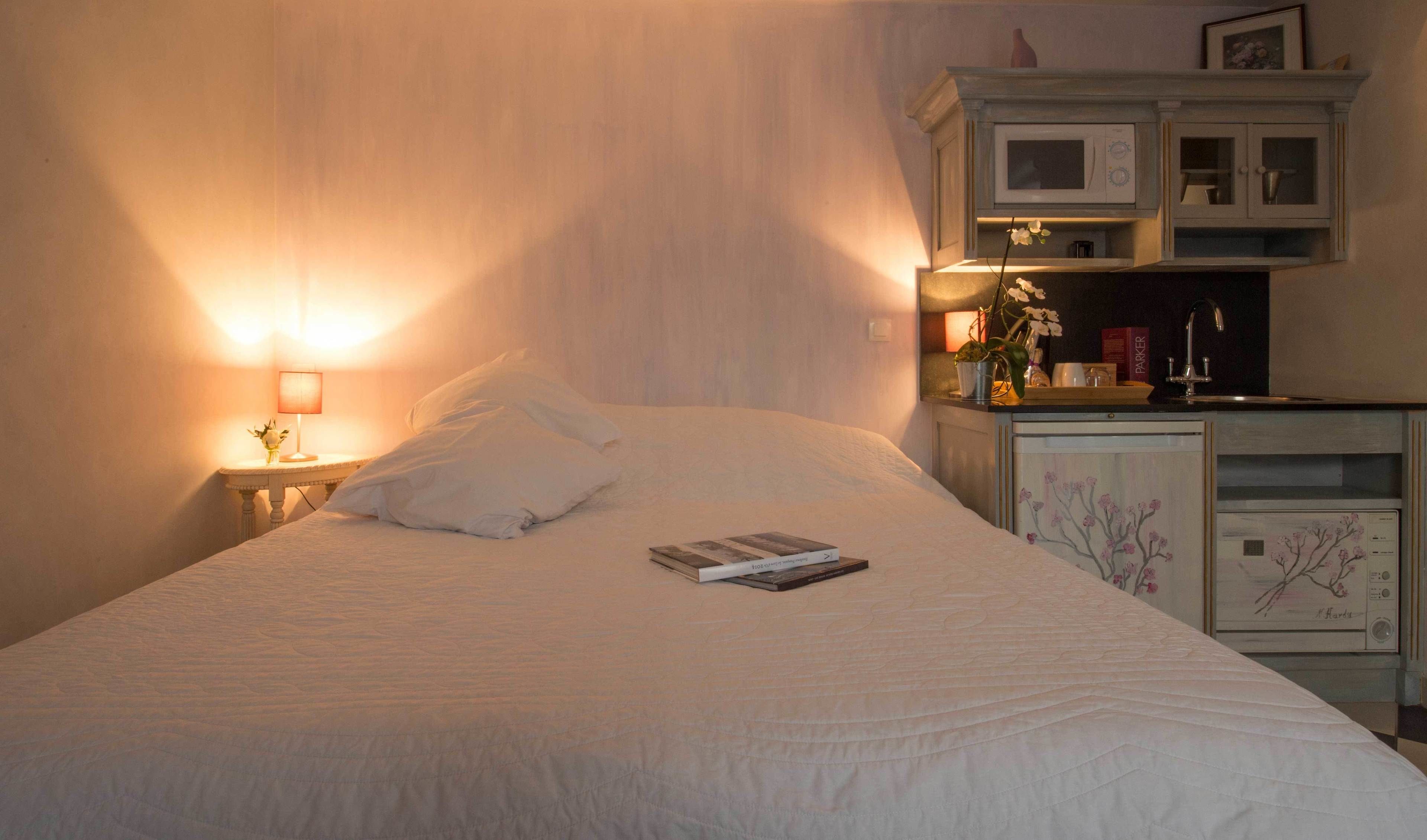 A neatly made bed with a book on it, a bedside lamp, and a microwave above a cabinet.