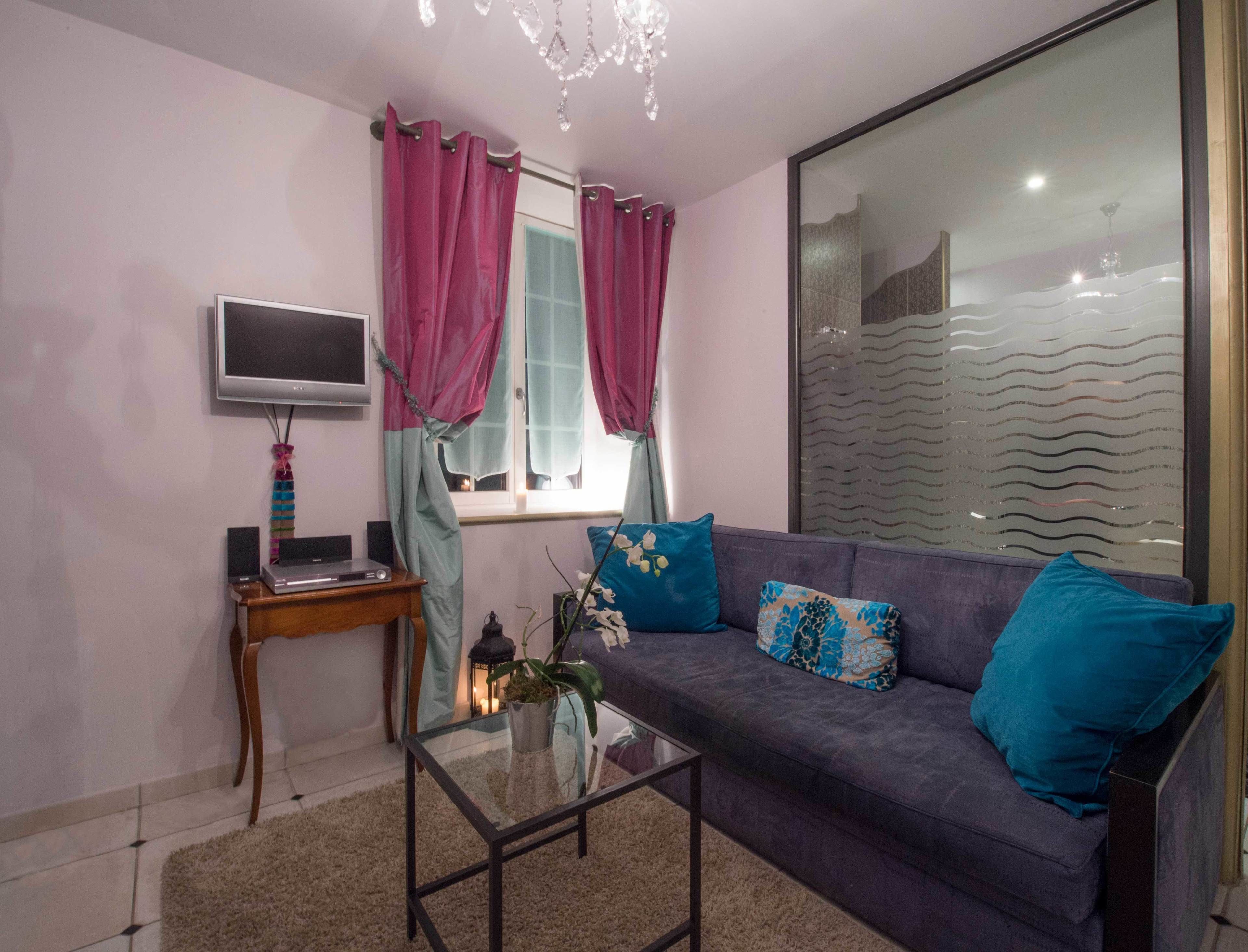 A living room with a sofa, a glass coffee table, a TV, and a window with curtains.