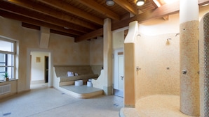A spacious indoor area with a large window, a stone fireplace, and a tiled floor. - ARAMIS Tagungs- und Sporthotel (Gaeufelden)