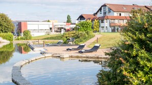A swimming pool area with lounge chairs, a small bridge, and buildings in the background. - ARAMIS Tagungs- und Sporthotel (Gaeufelden)