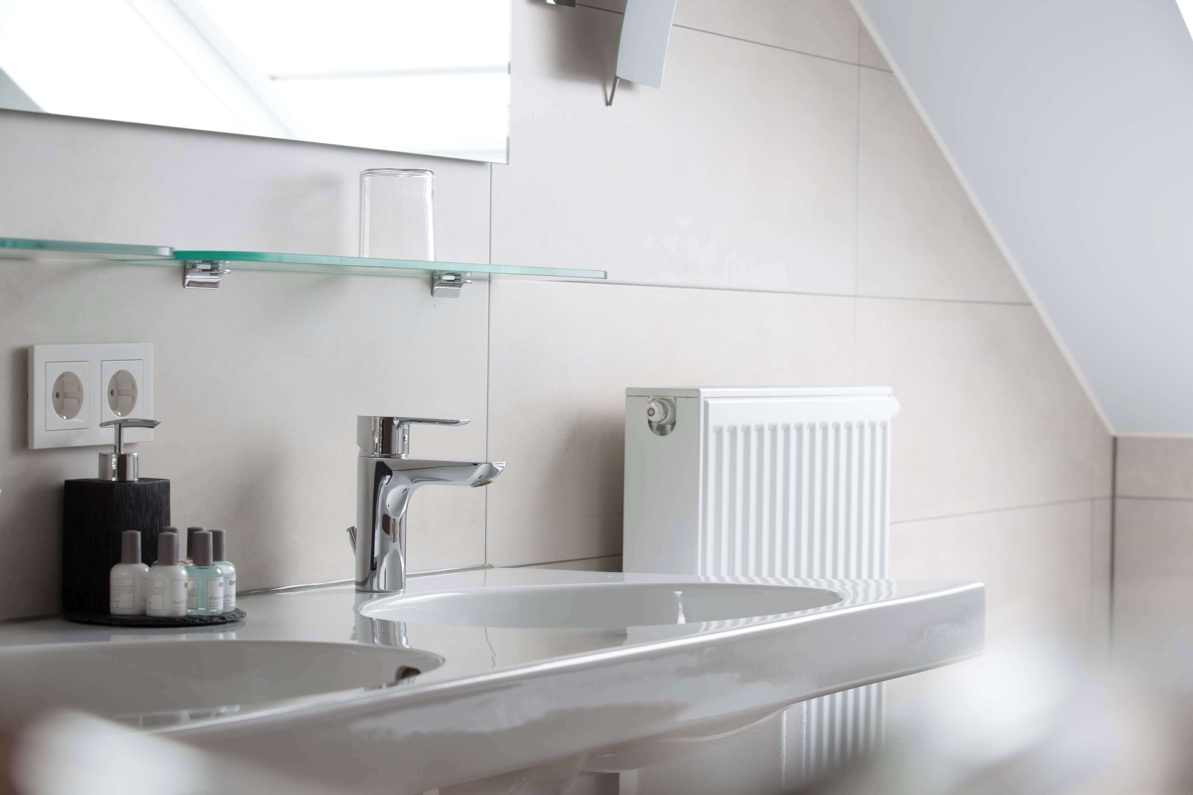Un baño moderno con un espejo grande, dos lavamanos y un estante de vidrio.