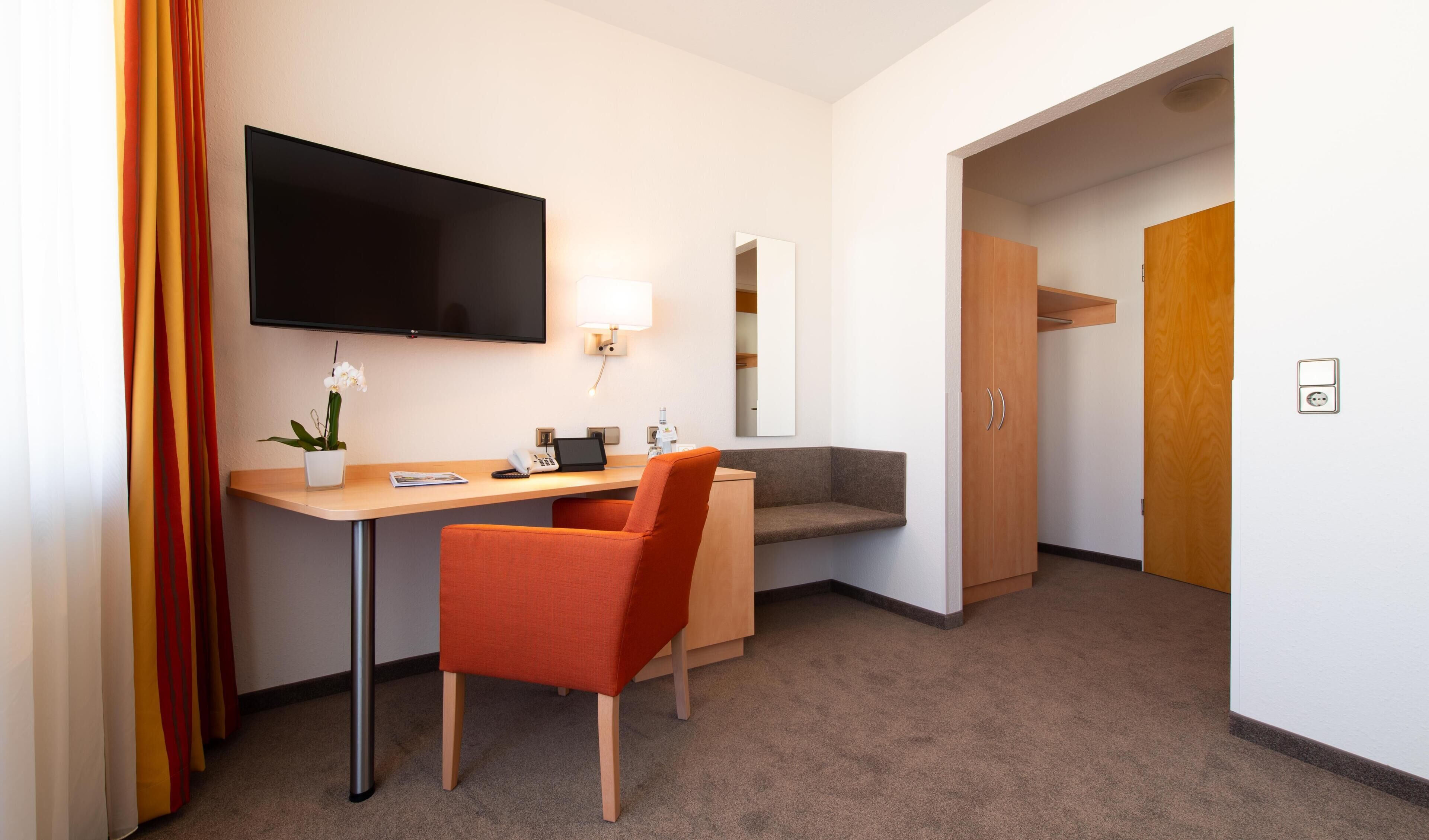 A hotel room with a desk, chair, TV, lamp, and a mirror.