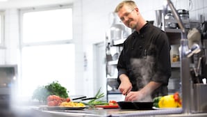 A chef cooking in a modern kitchen with stainless steel appliances and a large window. - ARAMIS Tagungs- und Sporthotel (Gaeufelden)