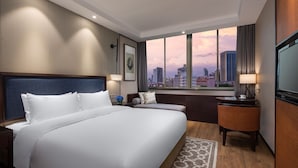 Une chambre d’hôtel avec un grand lit, un bureau, une chaise et une vue sur le paysage urbain par la fenêtre.