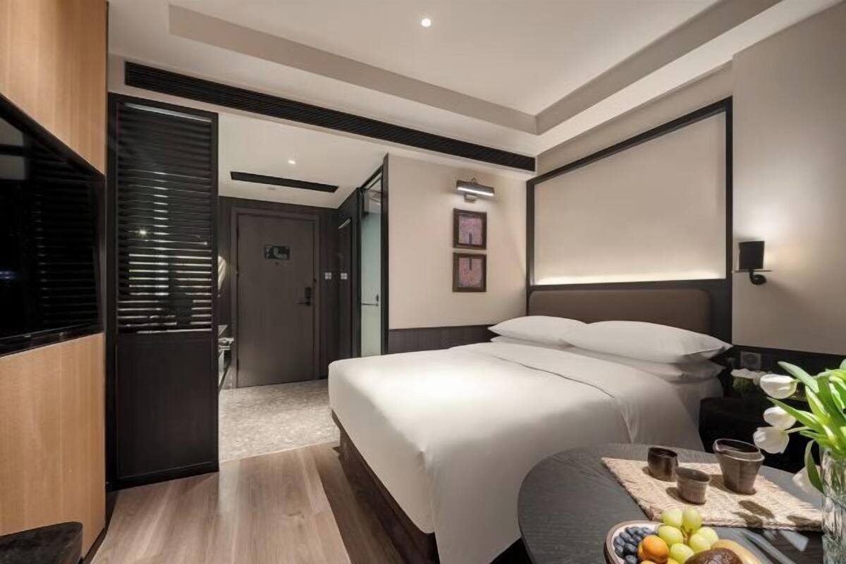 Habitación de hotel moderna con una cama grande, mesita de noche y una pequeña zona de estar con un frutero.
