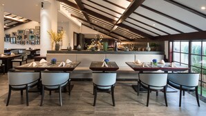 Un espace repas moderne doté de plusieurs tables et chaises, d’un comptoir de cuisine et offrant une vue sur l’extérieur.