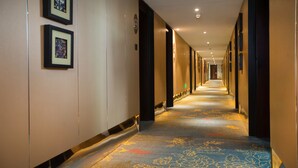 Un couloir d’hôtel avec des œuvres d’art encadrées accrochées aux murs, un sol recouvert de moquette et des portes donnant accès aux chambres.