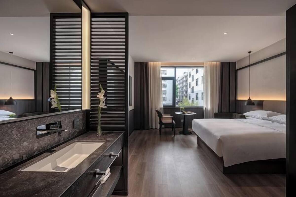 Una habitación de hotel moderna con una cama grande, baño independiente con bañera, una mesita y vistas a la ciudad.