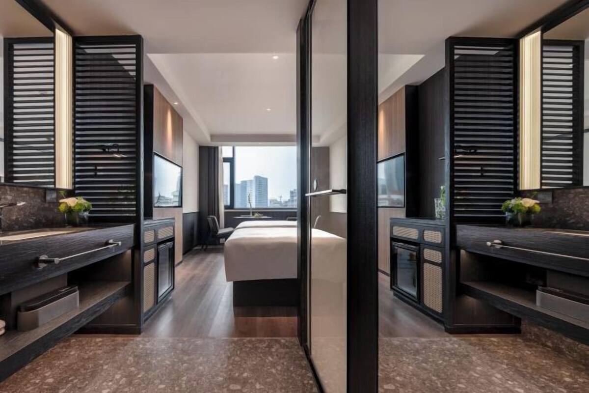 Una habitación de hotel moderna con una cama grande, dos mesitas de noche, un televisor integrado y vistas a la ciudad.