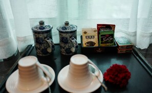 Deux théières en céramique, une boîte de café Nescafé, une boîte de thé PureTea et une fleur rouge sur un plateau.