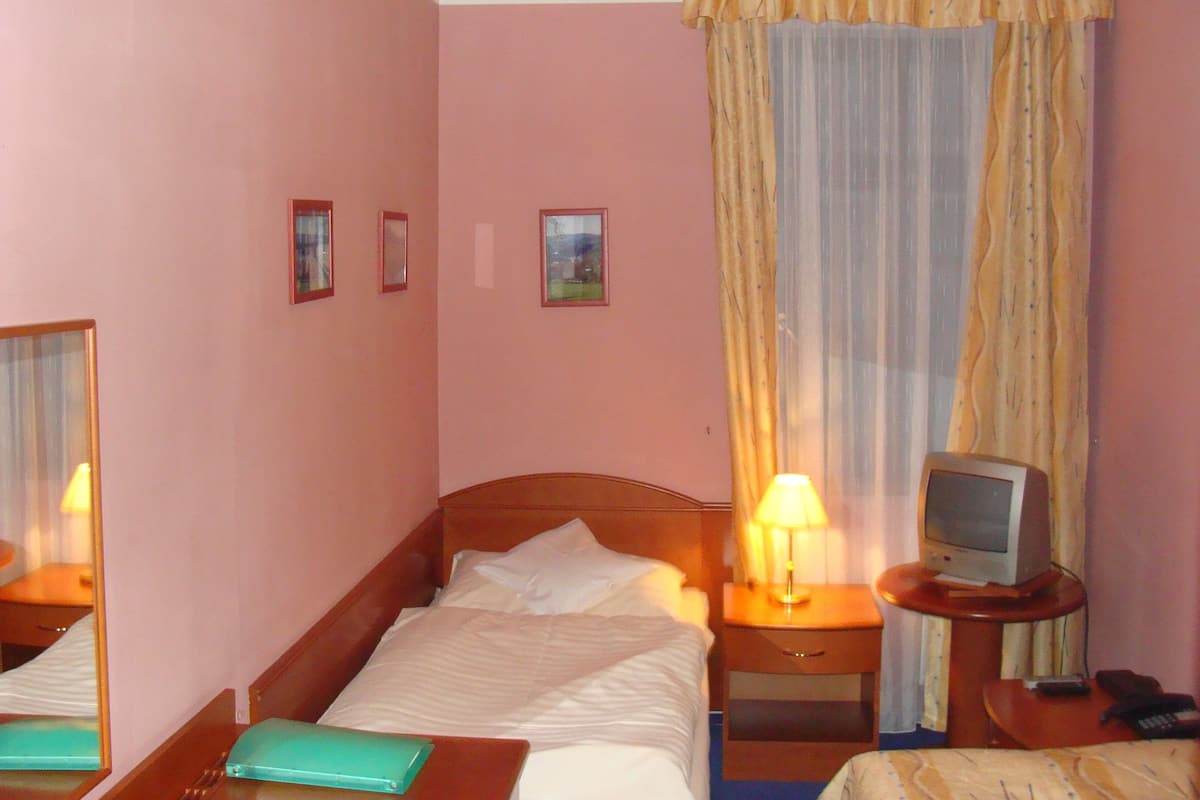 A hotel room with a single bed, a bedside table with a lamp, a television, and a small table with a remote control.