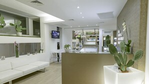 A modern reception area with a white reception desk, a seating area with white sofas, and a television mounted on the wall. - Villa Katy (Bardolino)