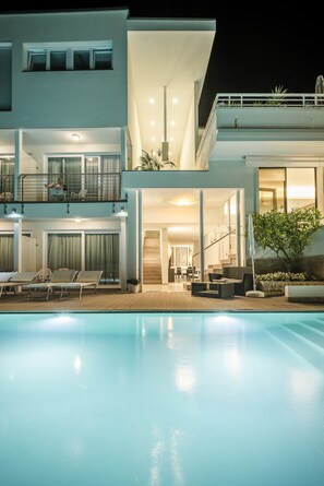 Un edificio moderno de dos pisos con piscina, mobiliario exterior y un balcón con barandilla.