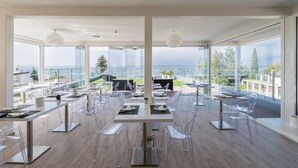 A modern dining area with clear chairs and tables, large windows offering a view of the sea and buildings. - Villa Katy (Bardolino)