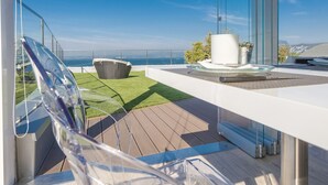 A modern balcony with a clear view of the ocean, a glass chair, a small table with a potted plant, and a grassy area. - Villa Katy (Bardolino)