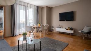 Una sala de estar moderna con comedor, un televisor de pantalla plana en la pared y un amplio ventanal con cortinas translúcidas.