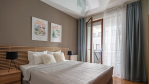 Un dormitorio moderno con una cama grande, cabecera de madera, dos mesitas de noche y vistas al exterior a través de un ventanal.