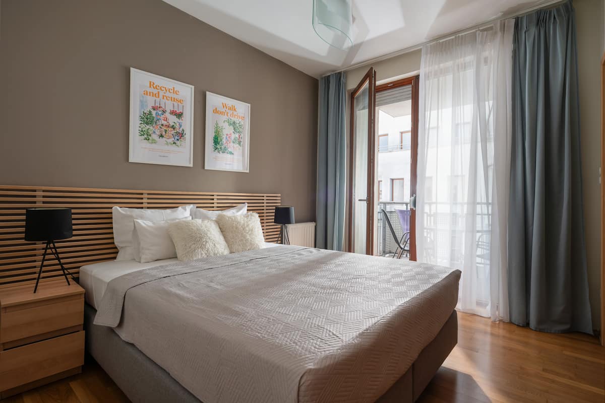 Une chambre moderne avec un grand lit, une tête de lit en bois, deux tables de chevet et une vue sur l’extérieur grâce à une porte vitrée.