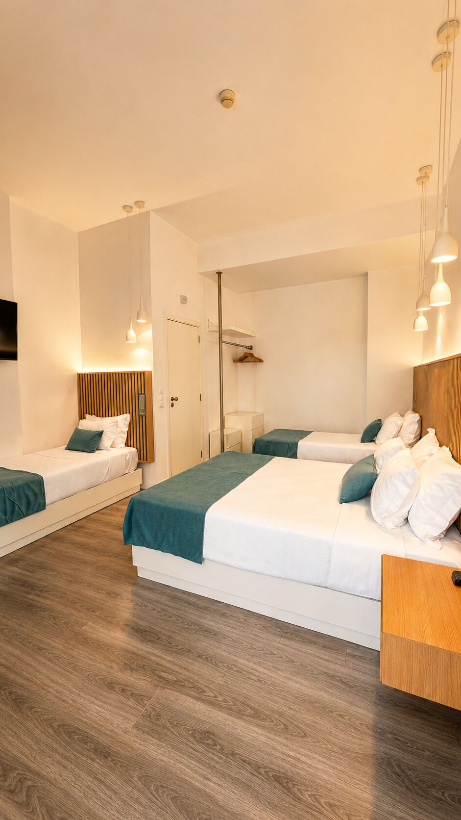 Une chambre d’hôtel moderne avec deux lits simples, une tête de lit en bois, un plancher en bois et des luminaires suspendus.