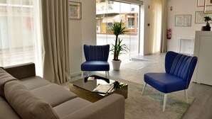 Un vestíbulo moderno con dos sillones azules, un sofá color beige y una mesa de centro de vidrio.