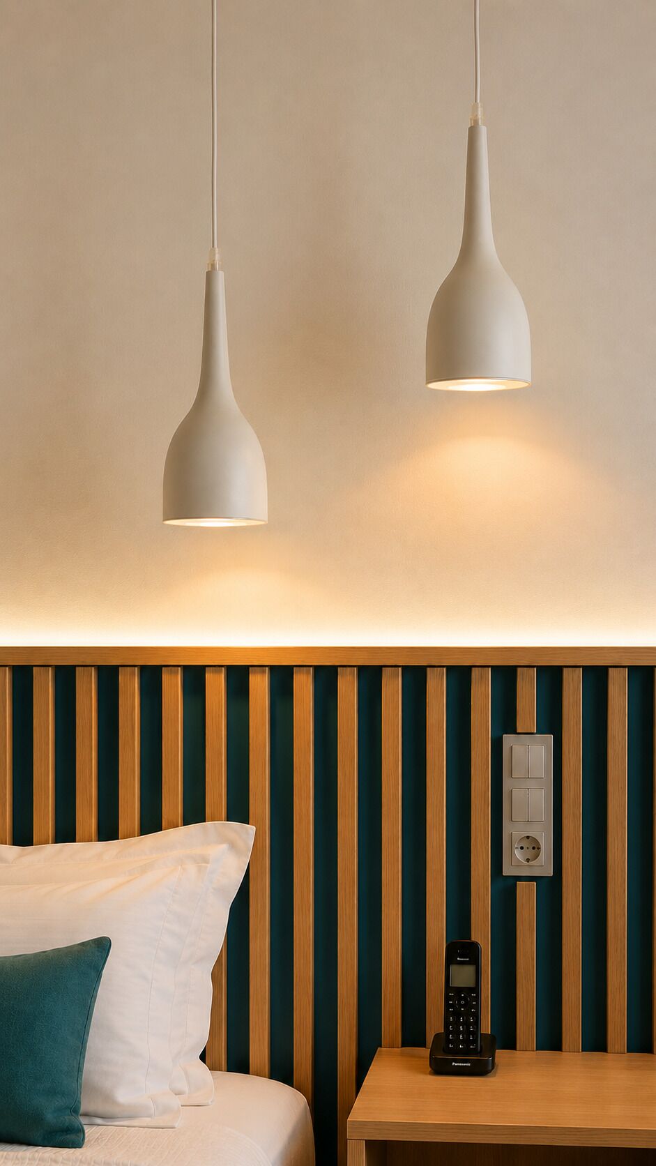 A hotel room with a bed, two pendant lights, a wooden nightstand with a phone, and a wall with vertical stripes.